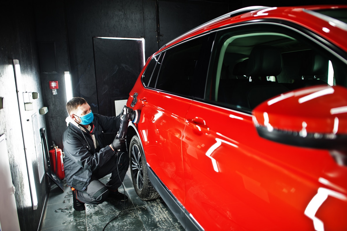 car detailing concept man face mask with orbital polisher repair shop polishing orange suv car 800 - АвтопластСервіс Одеса